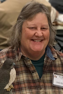 Cindy Roth smiles at the camera, next to a hawk carving